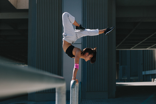 Sportswoman doing a handstand on railing outdoors. Flexible female athlete performing extreme sports in an urban space.