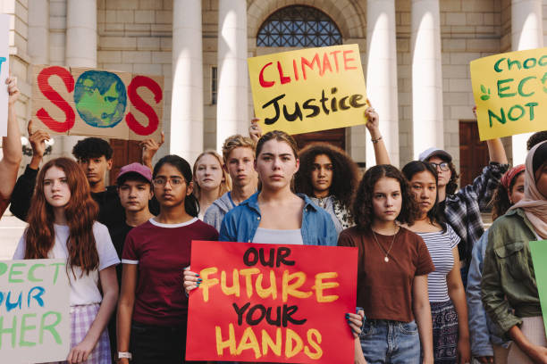 Multicultural teenagers holding a climate change demonstration Multicultural teenagers holding a climate change protest in the city. Group of youth activists holding banners and placards while marching for climate justice and environmental sustainability. climate justice stock pictures, royalty-free photos & images