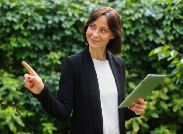 business woman uses a tablet against the background of green plants. portrait of a business woman with a tablet stock photo