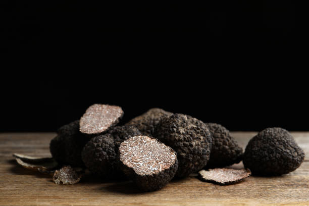 istock Whole and cut truffles on wooden table against black background 1415174717