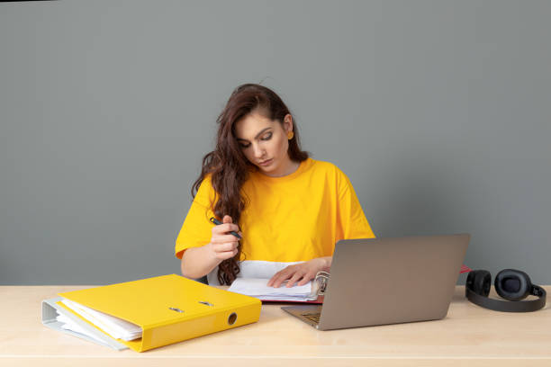 jeune femme d’affaires aux longs cheveux foncés travaillant avec un document au bureau, isolée sur fond gris - paper document pen long hair photos et images de collection