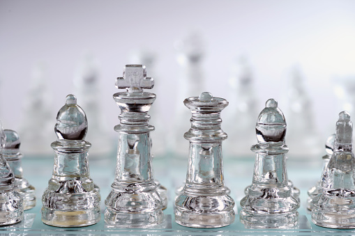 clear glass, transparent chess pieces on a checkerboard, selective focus, closeup, isolated on light