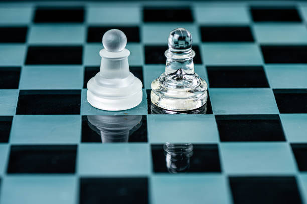 istock two opponent glass chess pawns on a glass chess board, black background 1415177814