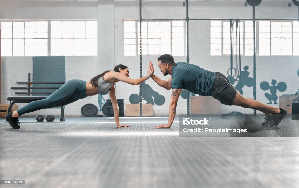 Fitness partners exercising together and doing pushups high five at the gym. Fit and active man and woman training in a health facility as part of their workout routine. A couple doing an exercise Gym Stock Photo