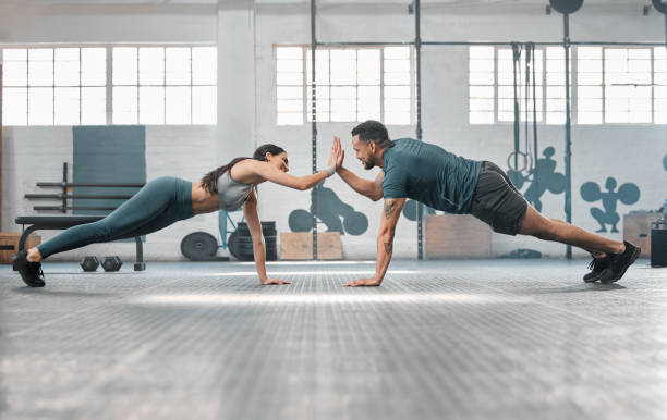 Fitness partners exercising together and doing pushups high five at the gym. Fit and active man and woman training in a health facility as part of their workout routine. A couple doing an exercise stock photo