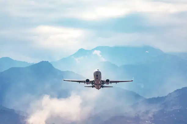 Photo of jet flight travel concept stock photo. Airplane fly above amazing blue misty mountain