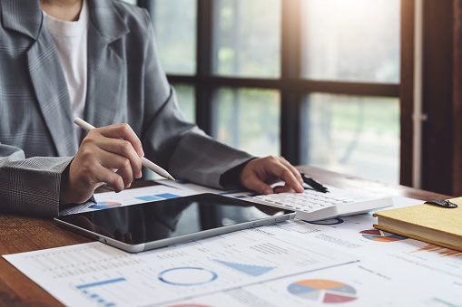 Business woman using calculator, tablet and documents to work.