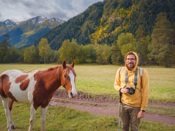 trip to Caucasus mountains, Arkhyz, Teberdinsky reserve. concept of discovery and exploration of wild places in early autumn. horse and hipster man in valley among autumn forest