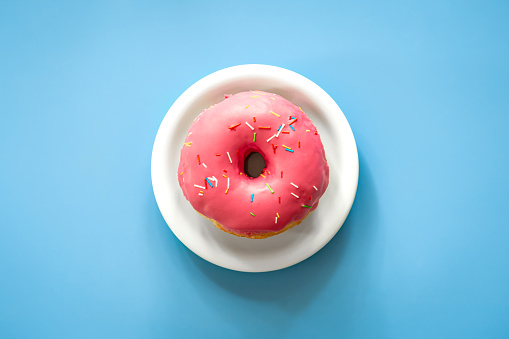 Donut with pink icing on a colored background isolated, conceptual minimalism.