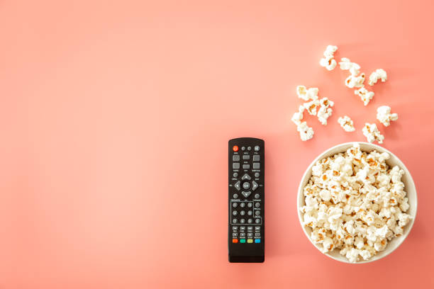 istock Remote control and plate with popcorn on a pink background, flat lay. 1415185870