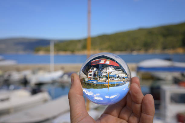 Hand holding glass sphere in the small harbor of Valun (Cres, Croatia), sunny day in springtime