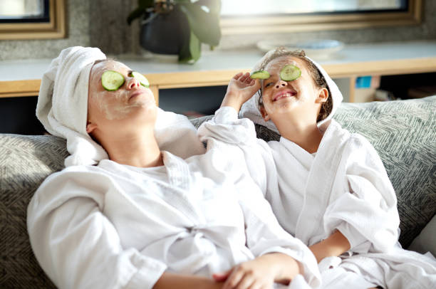 Fresh skincare, face mask and healthy skin treatment for bonding mother and daughter home spa day. Fun, smiling and playful child and parent relaxing with cucumber over their eyes in grooming routine