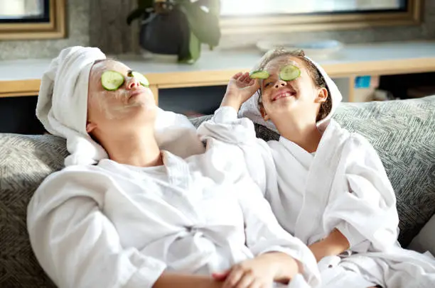 Photo of Fresh skincare, face mask and healthy skin treatment for bonding mother and daughter home spa day. Fun, smiling and playful child and parent relaxing with cucumber over their eyes in grooming routine