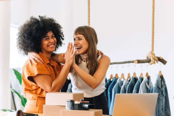 Cheerful online store owners high-fiving each other in their thrift store Cheerful online store owners embracing each other in their thrift store. Two happy businesswomen celebrating their success as a team. Female entrepreneurs running an e-commerce small business. high five stock pictures, royalty-free photos & images