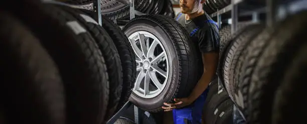 Photo of Hardworking experienced worker holding tire and he wants to change it In the tire store. Selective focus on tire.