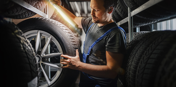 tire at repairing service garage background. Technician man replacing winter and summer tyre for safety road trip.