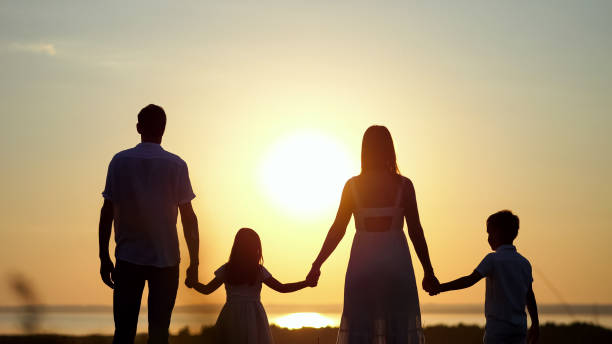 istock Family looks at sunset holding hands on meadow 1415194330