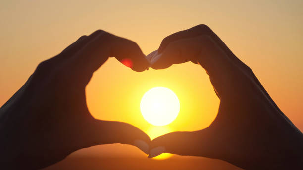 istock Woman makes big heart with hands at back sunset closeup 1415194364