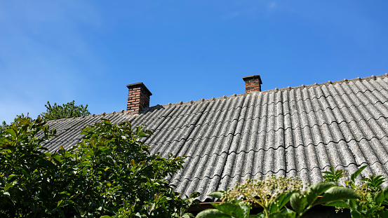 roof covered with old asbestos sheets and brick chimneys against blue sky