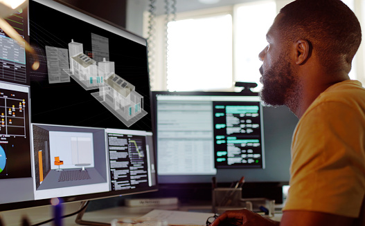 Stock image of an African American (Afro Caribbean) man working on a CAD design of a house with associated data on screen.