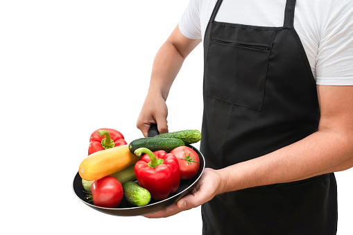 Frying pan with fresh vegetables in the hands of a cook isolated on a white background. Cooking concept.