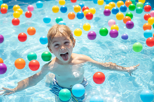 Young child, swimming in the summer in a pool full of colorful balls, enjoying beautiful sunny weather outdoors