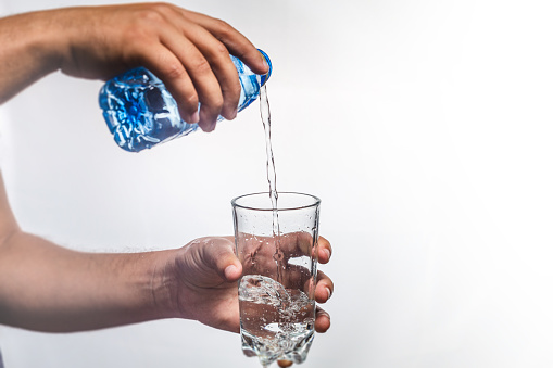 person pouring water in glass over white background - healthy lifestyle