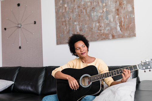 African American woman enjoying in playing a guitar at home