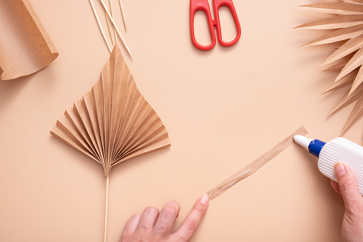 Applying glue to a paper strip for wrapping the trunk. Creative handwork to create tropical leaves. Master class.