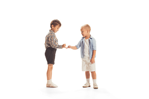 Portrait of two little boys, children playing together, making peace with fingers isolated over white studio background. Concept of childhood, game, school, fun, education. Copy space for ad