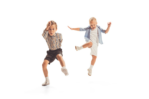 Portrait of two little boys, children playing together, running, jumping isolated over white studio background. Concept of emotions, childhood, game, school, fun, education. Copy space for ad