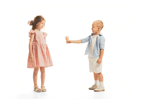 Portrait of children, little boy giving ice cream to beautiful girl isolated over white studio background. Concept of childhood, emotions, facial expression, game, fun, education. Copy space for ad