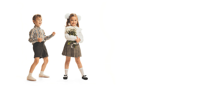 Portrait of children, boy in checkered shirt and girl with flowers posing isolated over white studio background. Retro fashion. Concept of childhood, game, school, fun, education. Copy space for ad