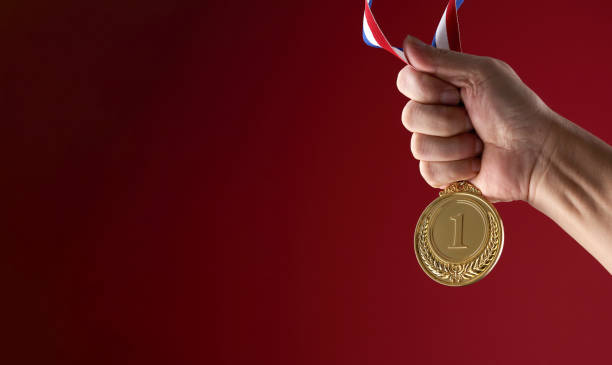 istock hand holding gold medal against red background 1415203708