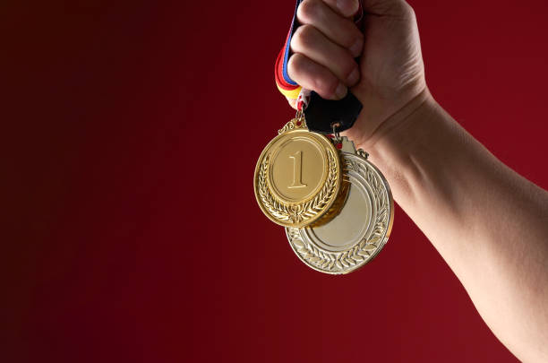 istock hand holding gold medal against red background 1415203725