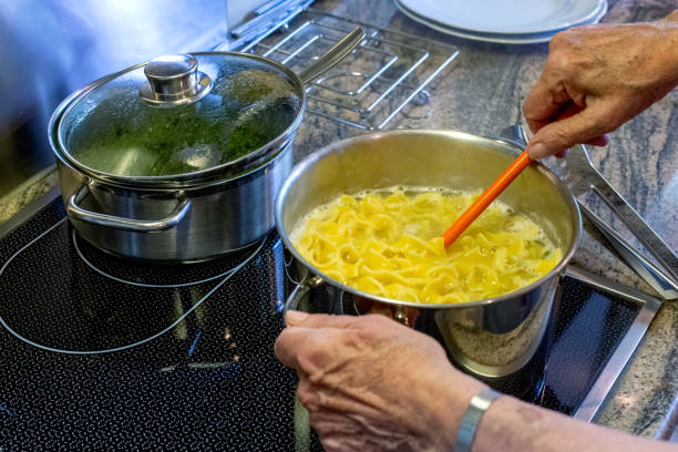 close-up de mãos de velhas e fogão com panela e macarrão - lifestyles domestic kitchen human hand furniture - fotografias e filmes do acervo