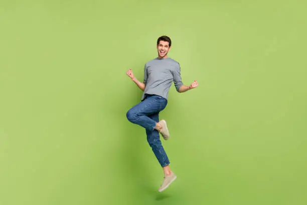 Photo of Full size photo of overjoyed ecstatic jumping positive man celebrate his victory isolated on green color background