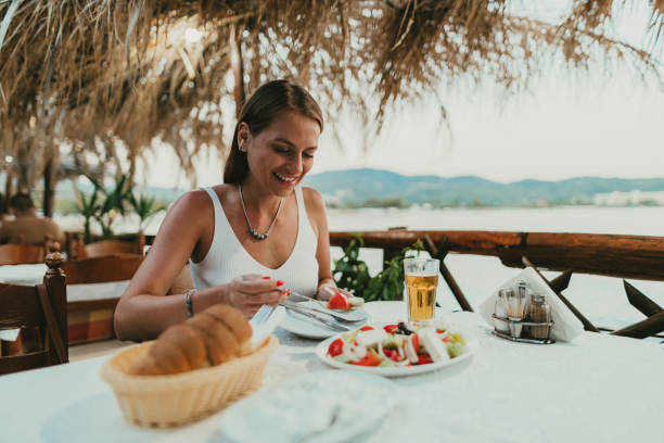 그리스의 해변에있는 레스토랑에서 그리스 샐러드를 먹는 여성 - greek cuisine greek culture food table 뉴스 사진 이미지