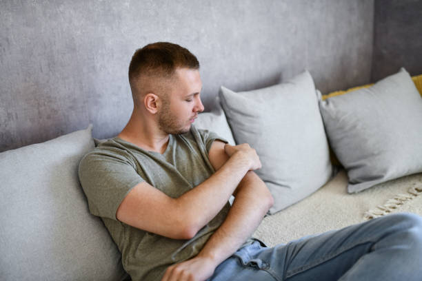 Male Picking At Scab With Fingers While Sitting On Couch stock photo