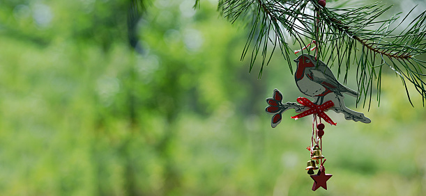 New Year's toy bird bullfinch made of wood with bells hangs on a pine branch on a green background. new year banner. copy space.