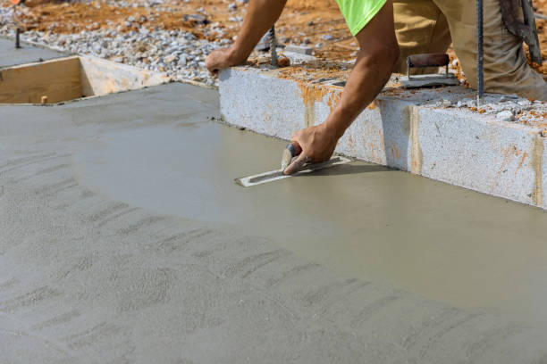 There is a masonry worker holding a steel trowel smoothing plastering concrete to a cement floor stock photo