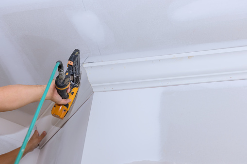 An air nail gun was used by carpenter to install the ceiling corner crown molding for new home