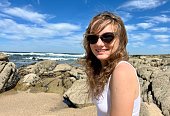 a teenage girl in sunglasses looks into the frame and smiles in the background she has the Atlantic Ocean in Portugal