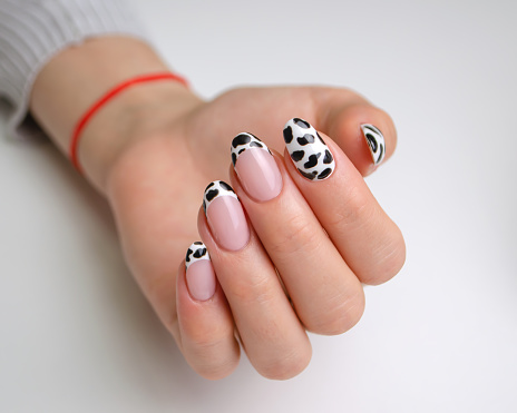 The hands of a young woman with a manicure. Nails are covered with gel polish with a French jacket and a black and white pattern