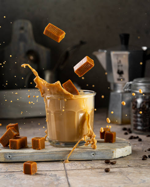 coffee with milk (caramel) splash in glass with toffee bites, flying food concept. - caramel latté coffee cafe macchiato imagens e fotografias de stock