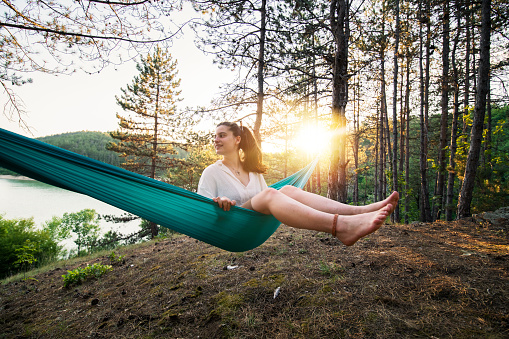 Young woman sitting in a hammock on camping vacation and enjying the beautiful nature on sunset.
