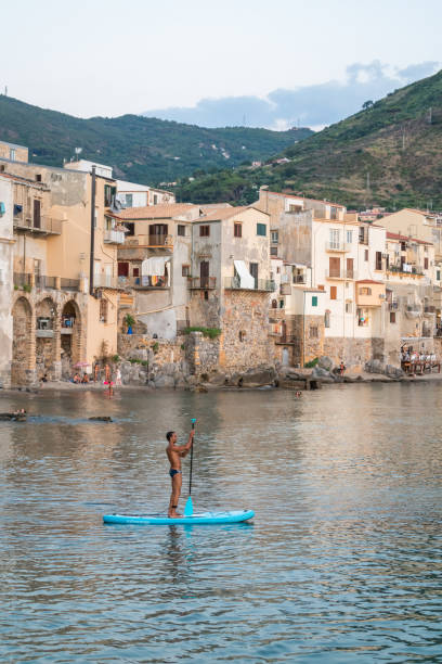 Cefalu Beach Cefalu, Sicily, Italy - July 11, 2022: A young man on sup board
at sunset on the city beach near the old town of Cefalu cefalu stock pictures, royalty-free photos & images