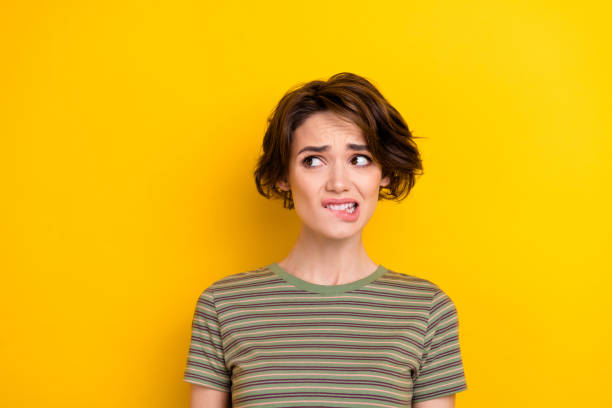 Closeup photo of unsure attractive girl looking empty space bit lip oops isolated on bright yellow color background Closeup photo of unsure attractive girl looking empty space bit lip oops isolated on bright yellow color background. gurning stock pictures, royalty-free photos & images