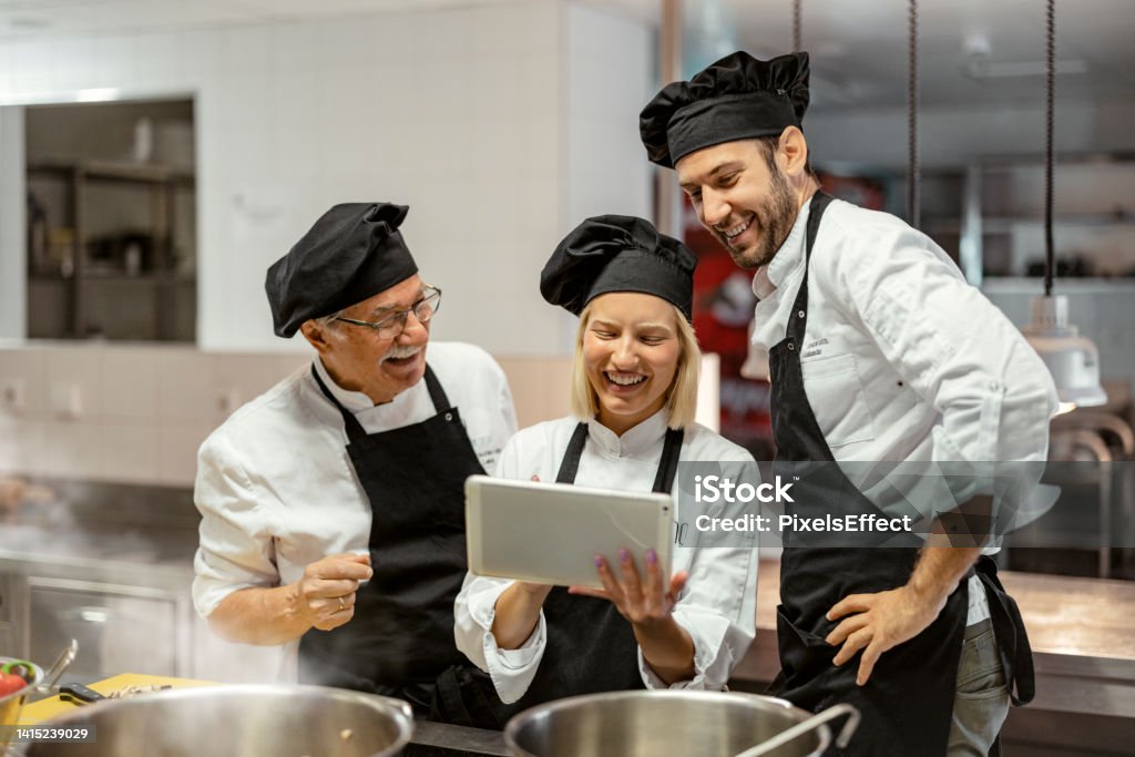 Wireless Kitchen Young female chef using digital tablet with her staff in a modern kitchen Chef Stock Photo