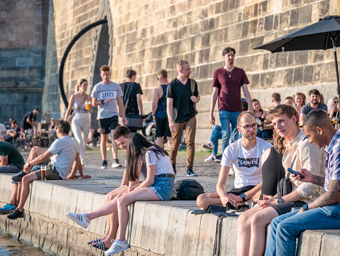 Prague, Czech Republic - June 2022: Tourists and locals sitting and having a beer on Naplavka along the Vltava river, in Prague